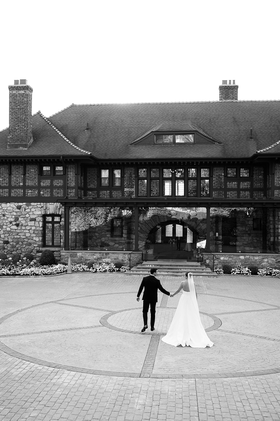 Black and white film photo of the couple walking hand-in-hand toward the grand historic Le Chateau mansion.